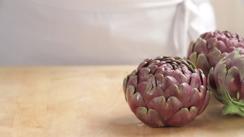 Removing leaf tips from artichokes and sprinkling the cut surface with lemon juice
