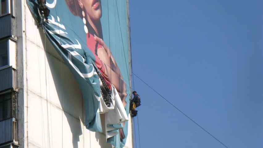 MOSCOW - MAY 16: (Timelapse View) Worker dismantles banner hanging highly on house wall, on May 16, 2012 in Moscow, Russia
