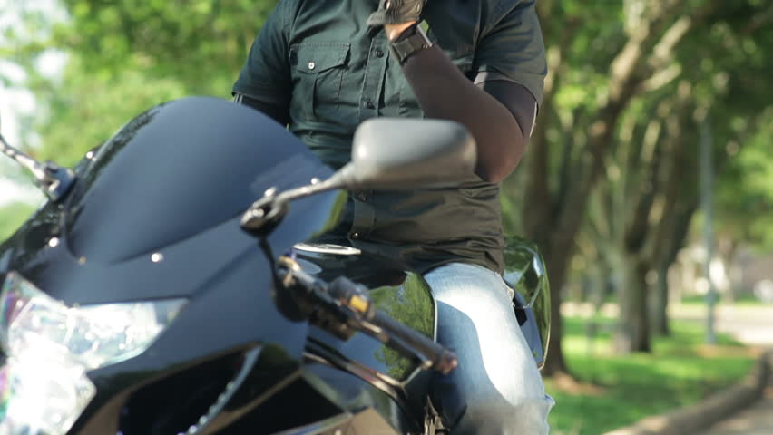A man sitting on his motorcycle with his visor open looks at his phone as if seeking information about his whereabouts.