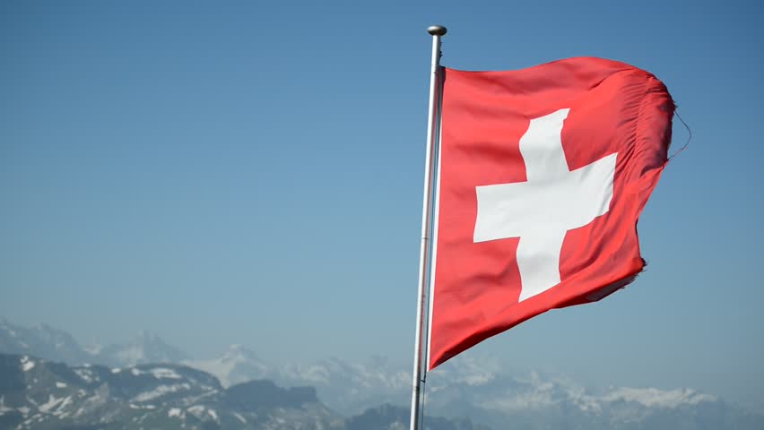 National flag of Switzerland waving in the wind with blurred mountains in the background. View from Brienzer Rothorn, Switzerland.