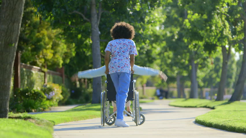 Nurse walking with elderly woman in wheelchair