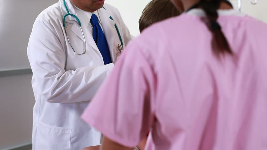Camera reveals from behind nurse to pediatrician giving instructions to her about boy patient care.