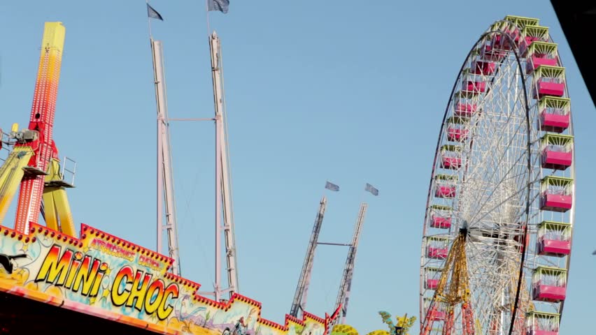 Ferris wheel and other attractions in an amusement park against a blue sky.