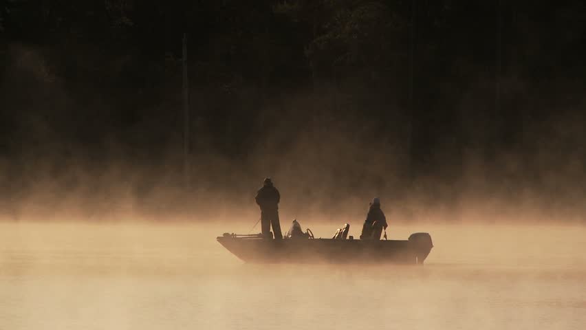 Fog rising from small pond at daybreak with men in small fishing boat 