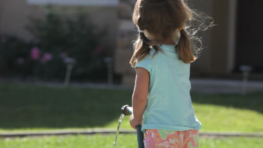  Cute little girl holding a water hose and shaking it as she waters the lawn 