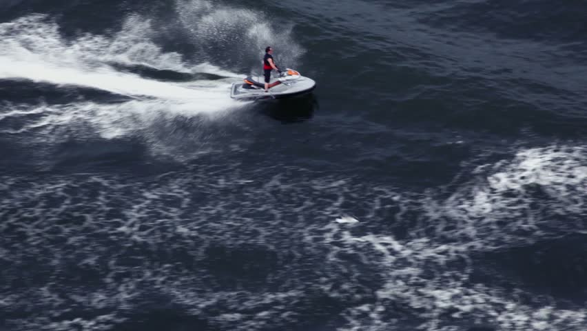 Man ride on water scooter in wavy sea and few gulls fly around