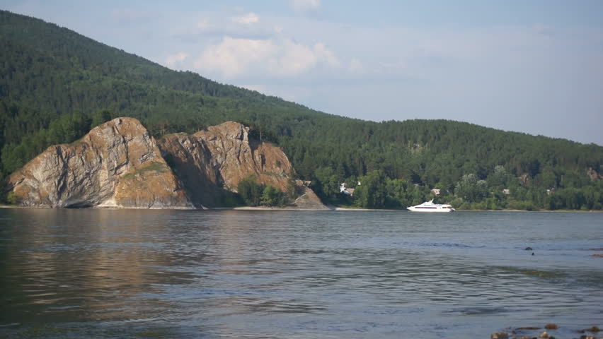 White pleasure boat push off from the mountainous coast of the Siberian river Yenisei. Static shot.
