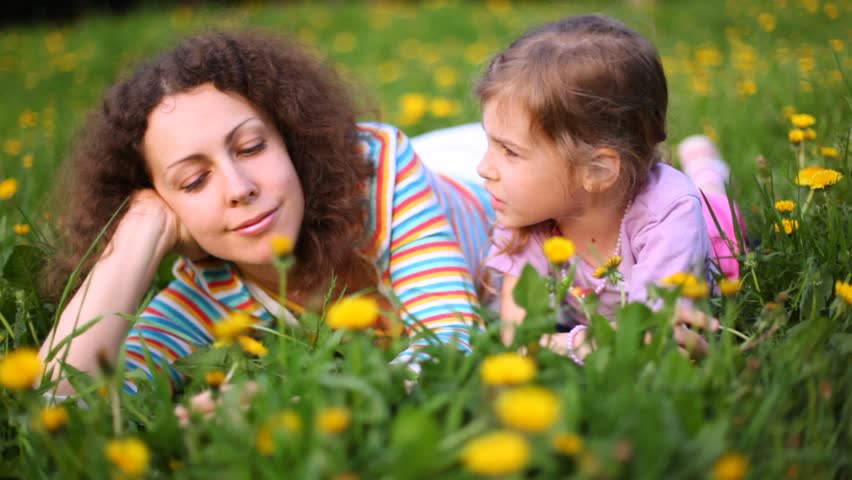 Mother and daughter talk on lawn with dandelions in sunny weather