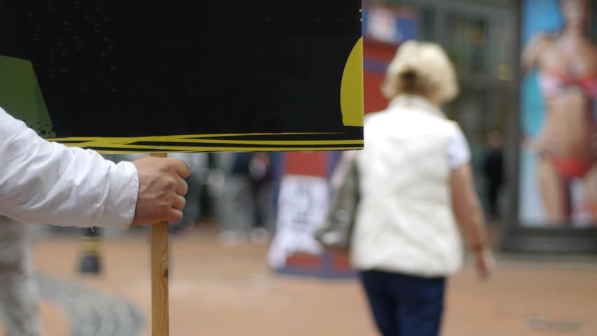 A man's hand holding a street sign. Out of focus people in the background.
