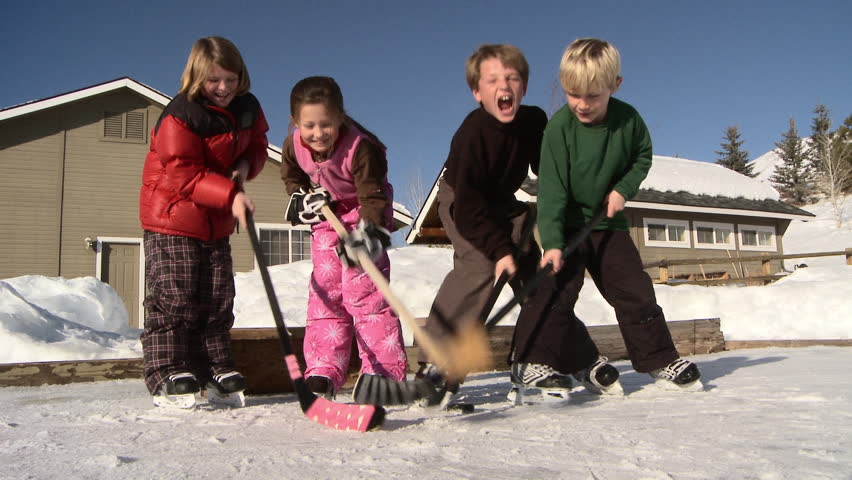 Four young kids bang their hockey sticks on backyard ice rink