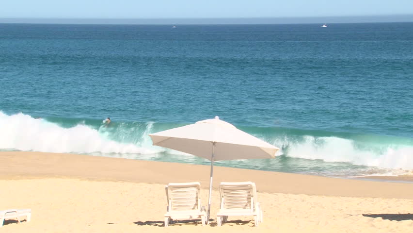 Unrecognizable people enjoy perfect blue sky day at the beach in Cabo San Lucas, Mexico by resort.