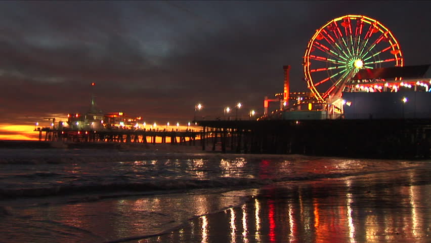 An early evening shot of the Santa Monica pier with its ferris wheel beautifully lit up , reflecting into the wet sand and gentle waves after the sun sets