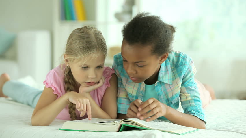 Little girls reading a book at home and chatting cheerfully