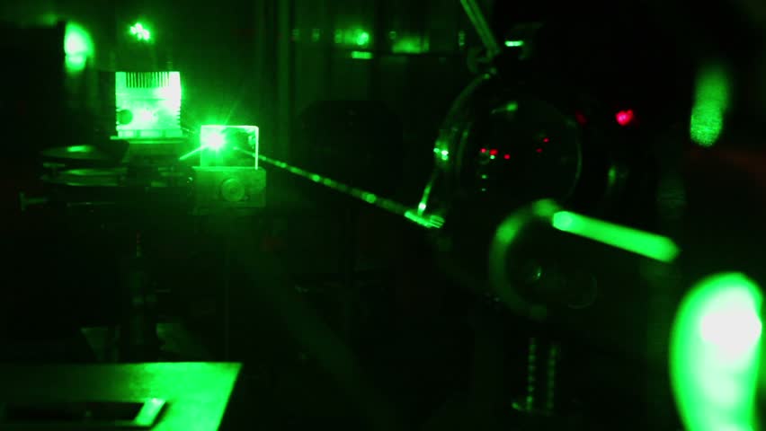 Glisten beam of green laser on table in dark laboratory