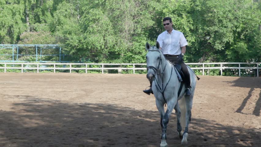 Jockey rides on horseback by equestrian field at sunny summer day