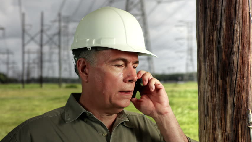 An electrical power grid repairman on the phone and smiles at camera.