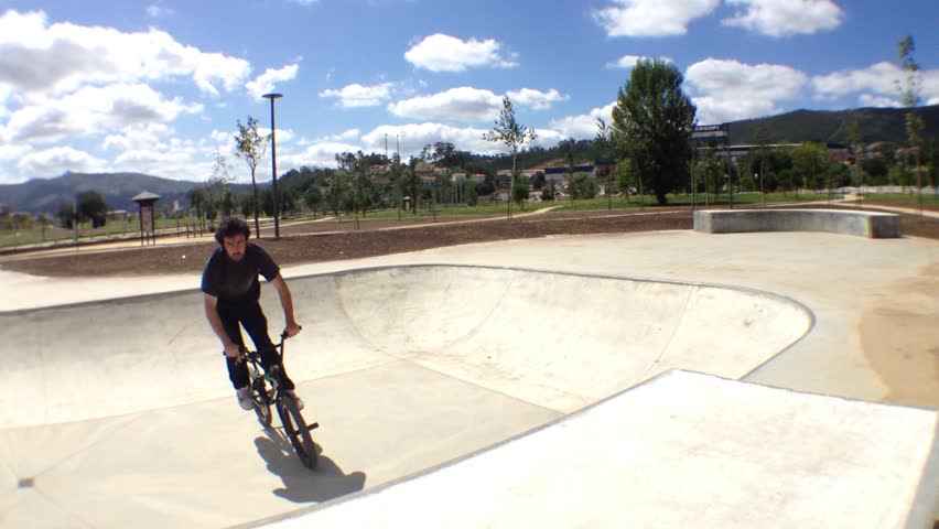 BMX bike stunts in skateboard park on a sunny day.
