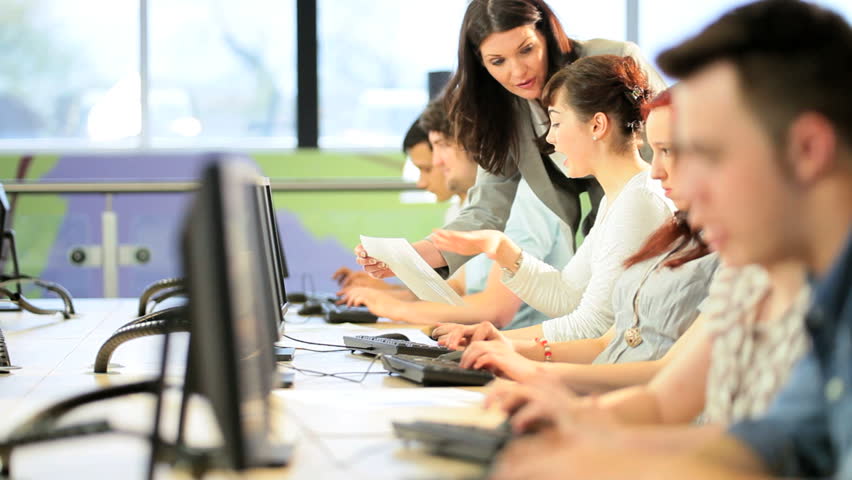 Female and male diverse classmates focus on university project with young Caucasian teacher in campus computer room