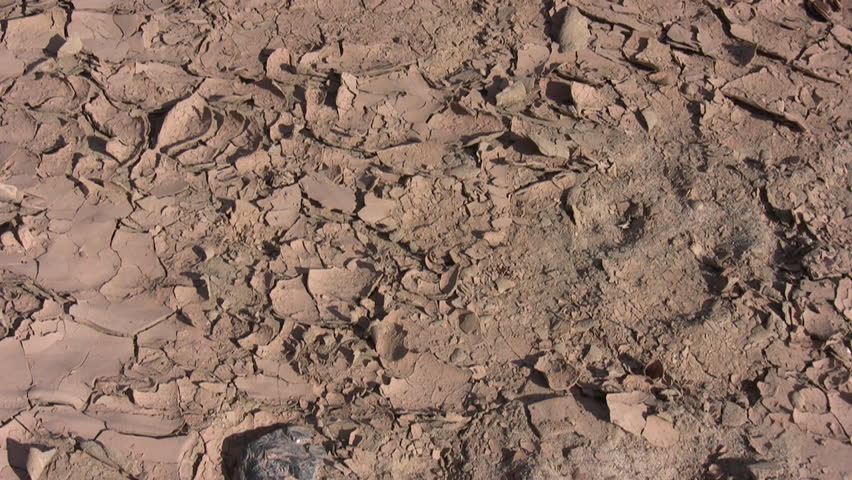 HD pan up of the cracked mud along a dry river bottom to a small water-filled branch of a river