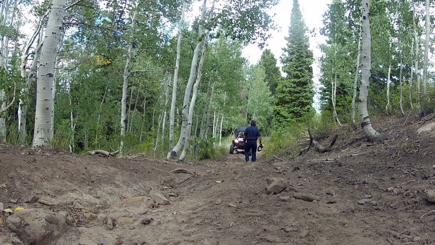Man on mountain getting in ATV sport utility vehicle. Explores the outdoor Rocky Mountain Wasatch range. Forest with Aspen and pine trees. Sport utility vehicle recreation, transportation and fun.