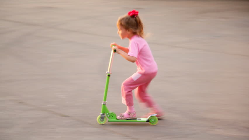 girl in pink goes for ride on green scooter, passing by other people