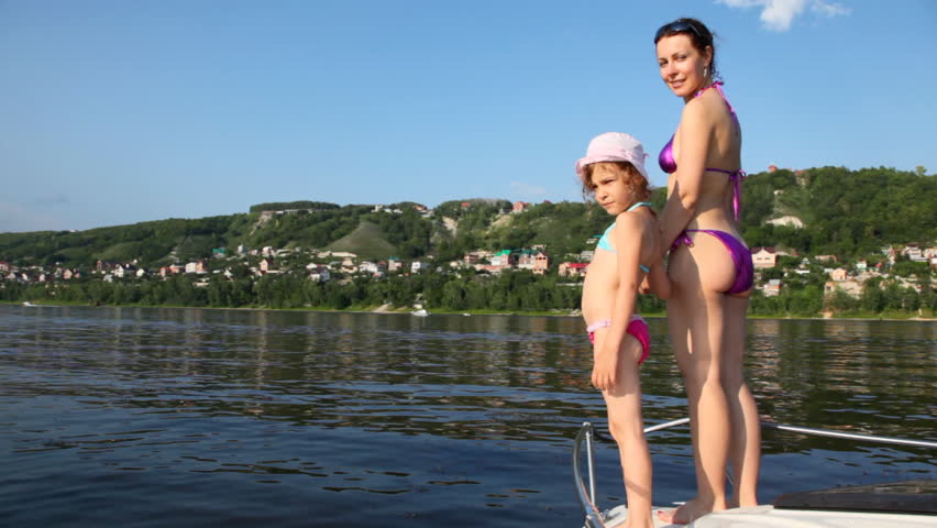 mother with daughter in bathing suits stand on yacht nose, hold hands and look in distance
