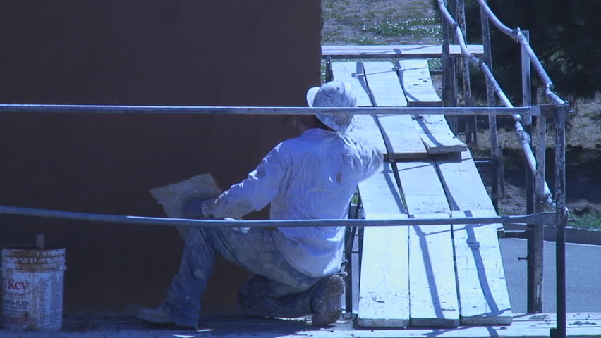 Stucco worker applies skin coat to building wall using trowel