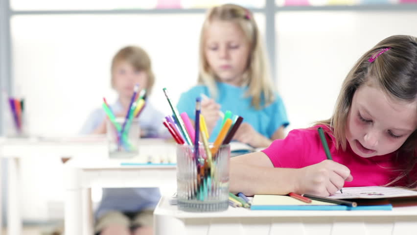 Cute little kindergarten child working at her desk is final focus of camera dolly movement.
