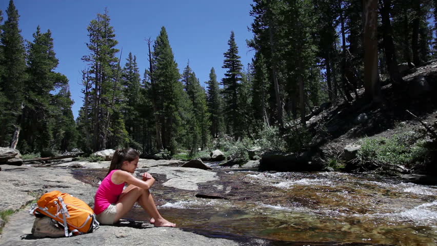 Hiker resting at water stream in Yosemite national park during hiking trek in forest.