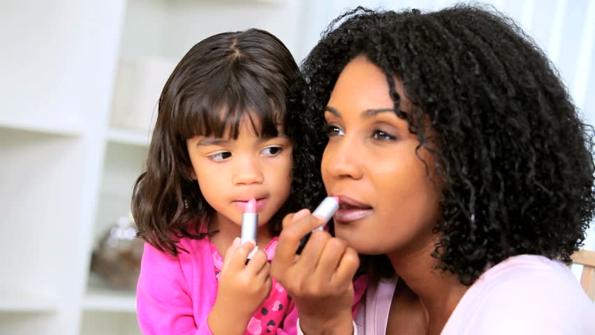 Attractive young ethnic mother with pre school daughter copying her using cosmetics