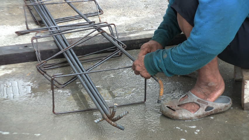 An old Asian man ties wire onto rebar to prepare forms for concrete in Bangkok, Thailand.