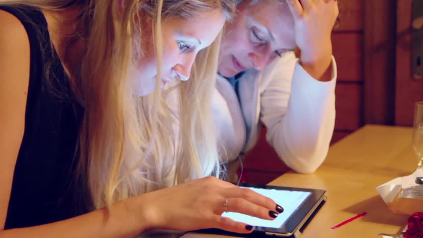 Two women use tablet pc at wooden table, closeup view