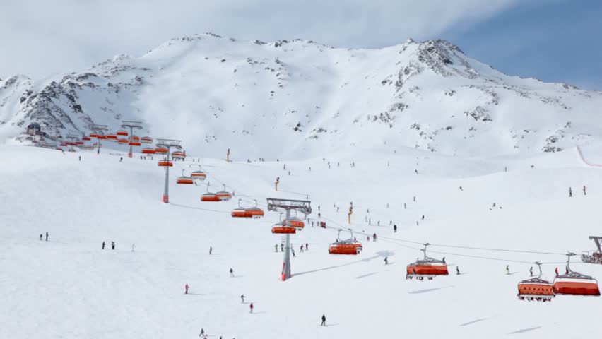Many skiers ride in Alps near cableway at sunny winter day