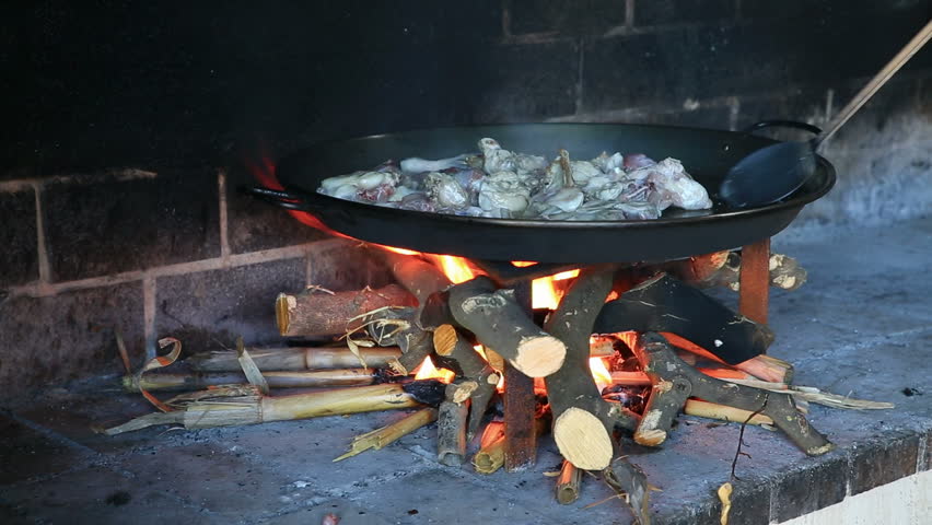 preparing large dish of paella with firewood, frying chicken