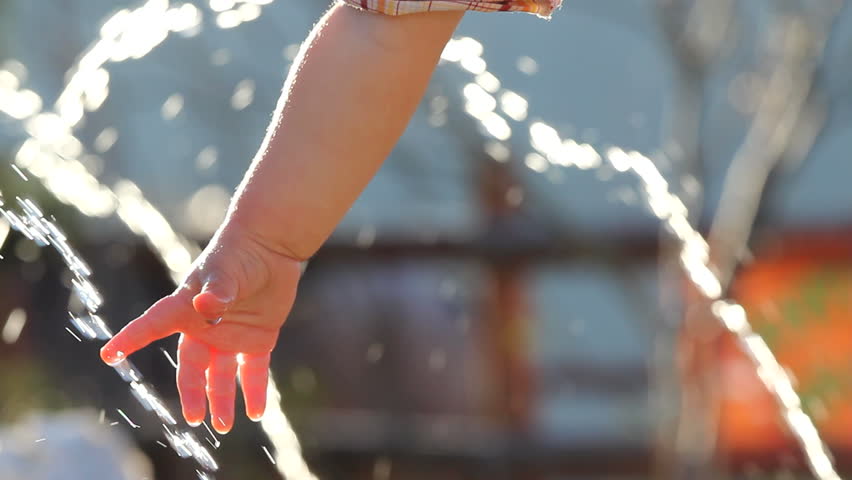 Baby hand touching and feeling the clear water drops from a fountain