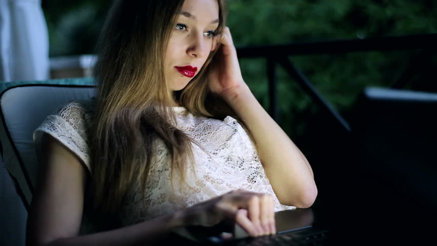 Young woman with laptop sitting on her balcony in the evening
