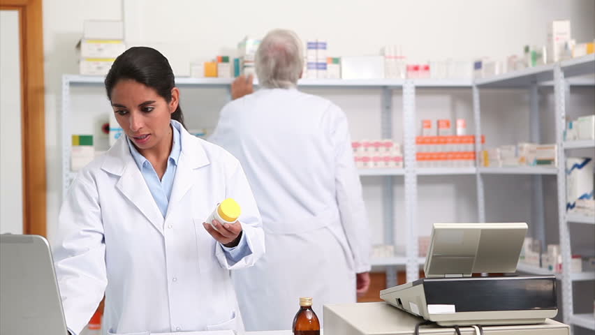 Female pharmacist holding a drug box while smiling in hospital ward