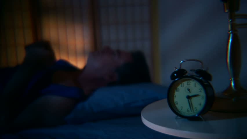 Man tossing and turning and having a restless sleep. Focus on the clock. Shot with a 35mm adaptor for shallow DOF and film look. 