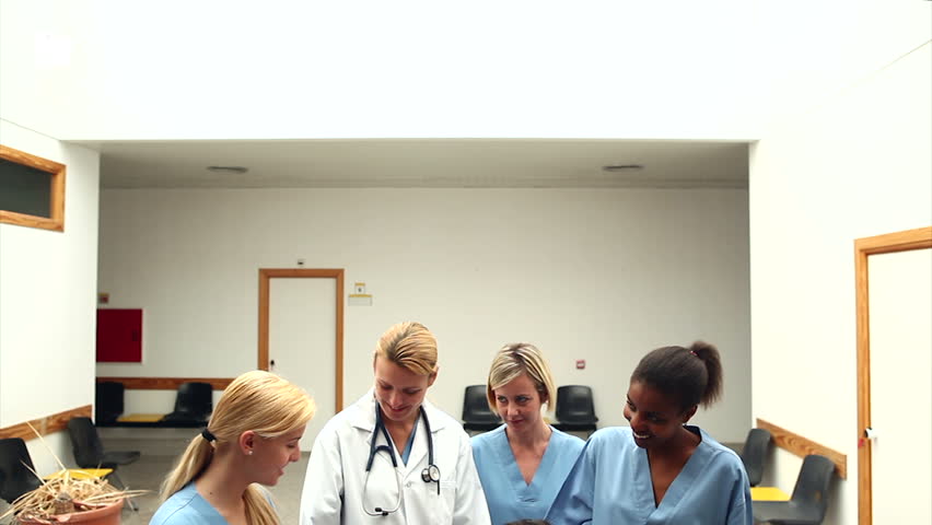 Smiling couple with their newborn baby surrounded by a team of doctor in the hallway of a hospital