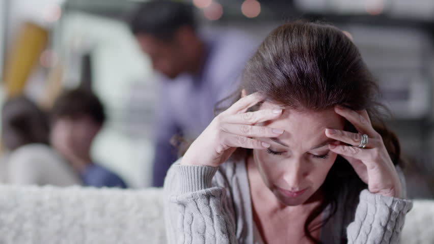 An attractive caucasian woman is upset and stressed about events in her life which are beyond her control. Her husband and children are unaware of her anxiety. In slow motion.