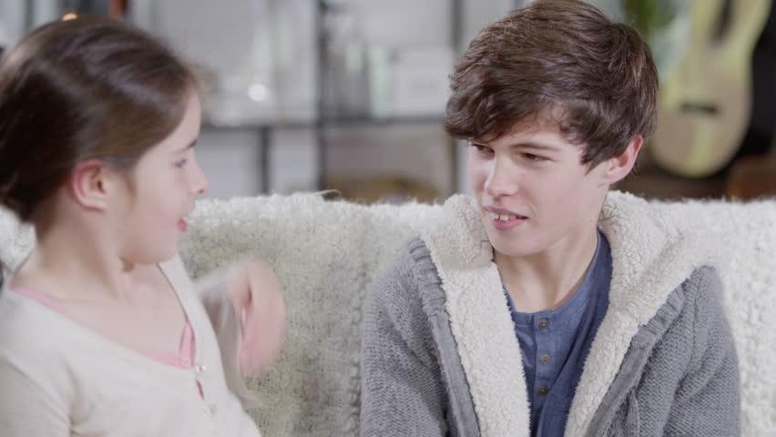 A young girl gives her brother a hug but he pulls away when she gives him a kiss! They both look directly into camera. In slow motion.