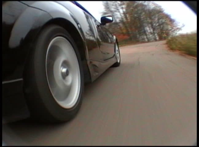  Black sport car in motion by the road. View from on-board camera on weel and wing 