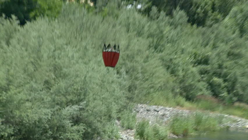 This shot opens with a medium-close shot of the bucket as it is lowered into the river, and then zooms out to include the surrounding area and the chopper as it starts to fly away.