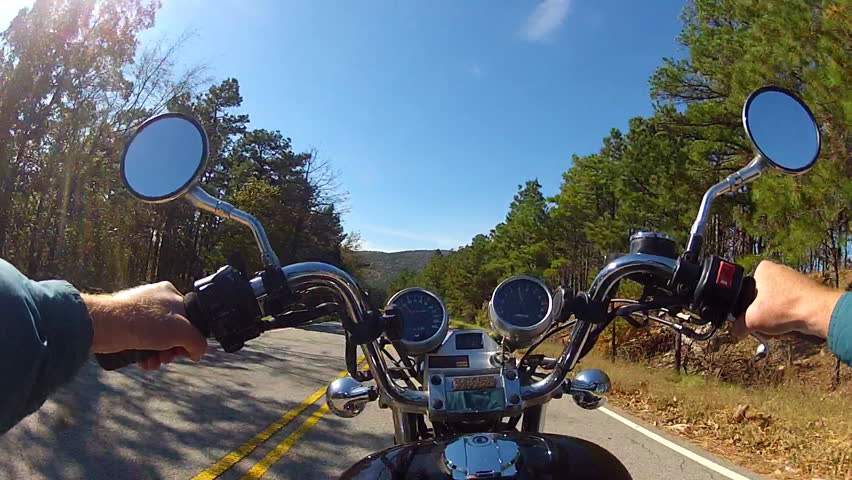 A wide angle point of view shot from a chest mounted camera on a motorcyclist riding a motorcycle on a forested mountain road.