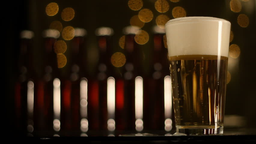 Stock video of beer being poured into glass, defocused background of lights and beer bottles