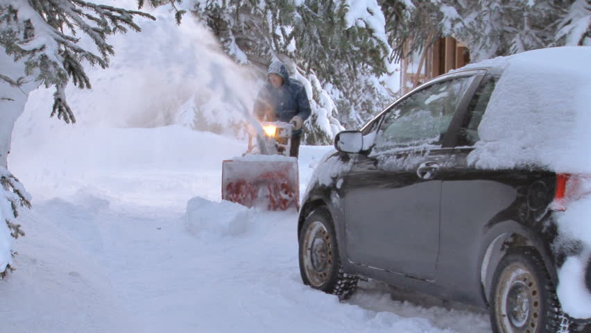Winter-garbed man clearing his driveway of snow with a snow blower. .