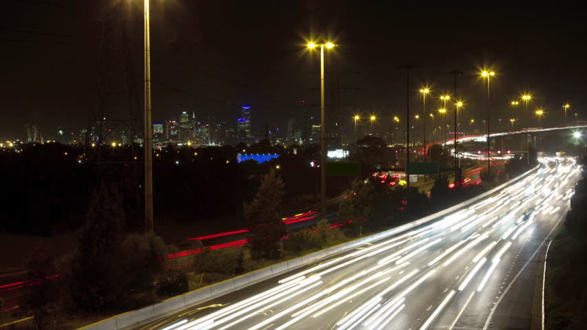 Timelapse at night of busy traffic on freeway with bridge & Melbourne no signs