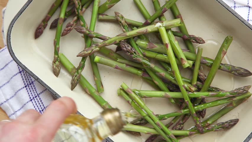 Green asparagus in a roasting tin being drizzled with oil