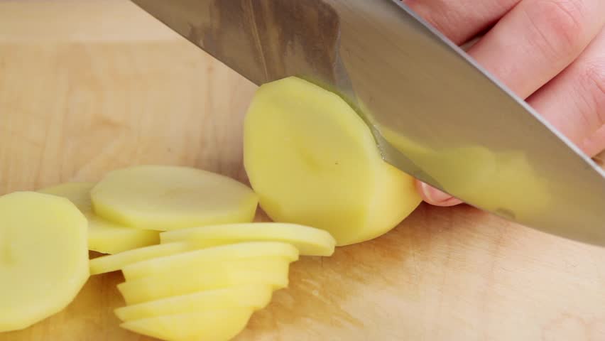 Peeled potato being thinly sliced (close-up)