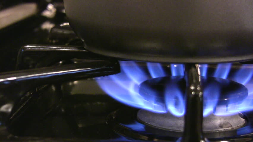 HD 1080i slow pan of a stainless steel pot warming over the blue flame of a gas stove.